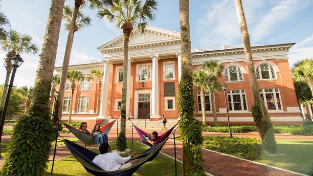 Students lying in hammocks outside of Sampson Hall on campus.