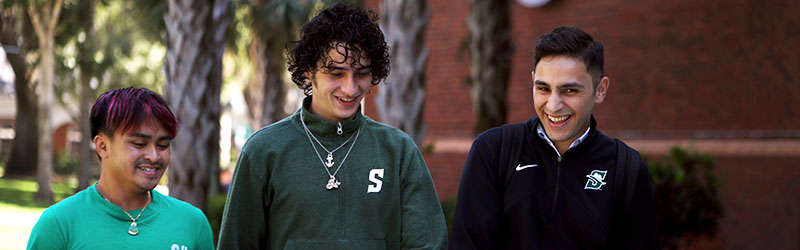 three students walking around campus and smiling together