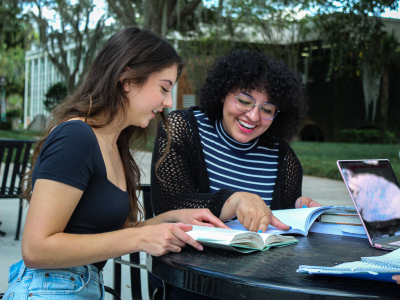 two girls sitting next to each other looking at a book