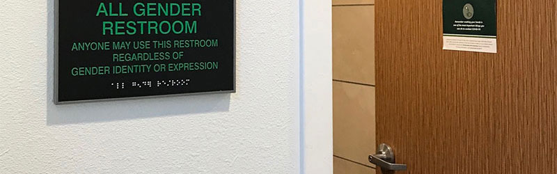 An all gender restroom sign next to an open door of a restroom.