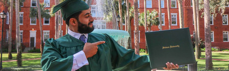 A graduating student pointing at their diploma in hand in the Palm Court