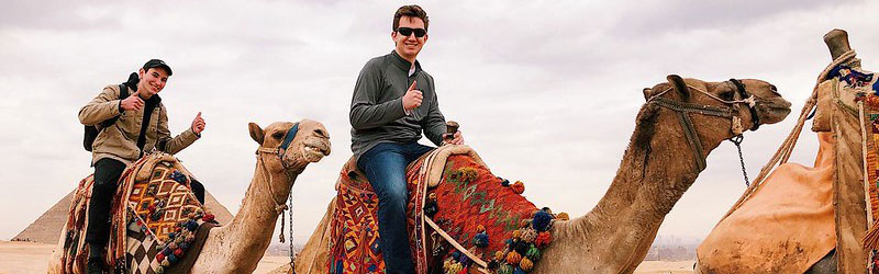 Students riding camels in front of they pyramids in Egypt.