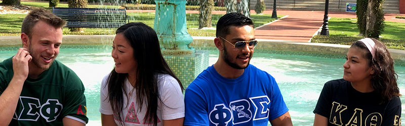 four students from different greek organizations sitting in front of fountain