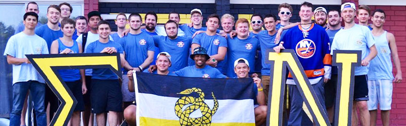 students from fraternity posing and smiling together holding their sign and flag