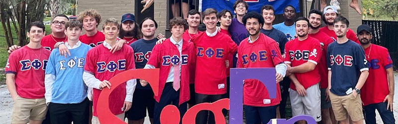 students from fraternity posing and smiling together holding their sign