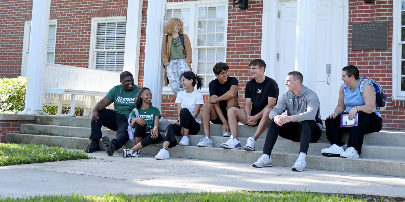 8 students sitting on the steps of a building hanging out together