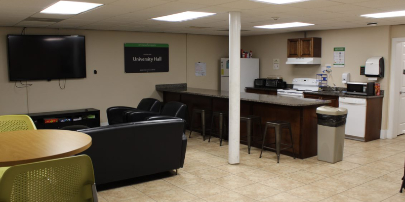 Kitchen of University Hall, with a TV, sofas, tables, chairs, stove, oven, fridge and microwave