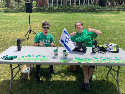 two people posing in front of a table with the flag of Israel