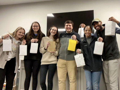 Six people posing together at they hold bags and smile for a service opportunity