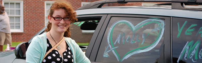 A commuter student happily posing in front of their car.