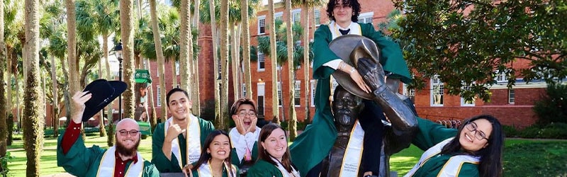 group of students smiling with their caps and gows sitting with John B