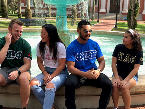 2 girls with their sorority shirts and two guys with their fraterninity shirts sitting in the fountain