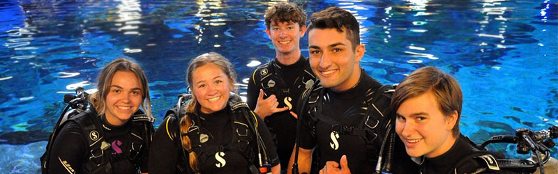 four students smiling on their scuba garments before a dive