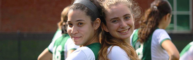 two girls smiling back to back with their soccer uniforms 