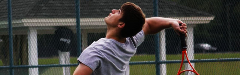 student jumping to hit tennis ball