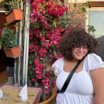 Gelly is wearing a white shirt in front of pic flowers.