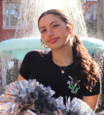 Juliana is standing in front of a fountain smiling.