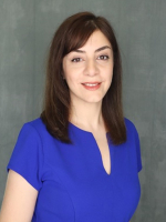 Woman in blue blouse smiling in front of a grey background