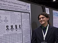 A student smiling while standing next to a poster of his research