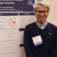 A student smiling while standing next to a poster of his research