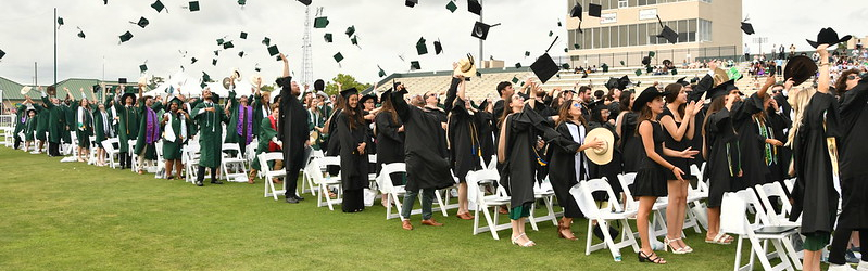 a large group of students in an open stadium throwing graduation caps into the air