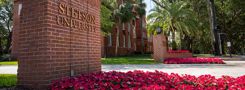 a brick sign saying stetson university with flowers in foreground and a brick building in background