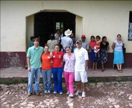 A group of individuals in front of a building entrance, with some people standing in the doorway in the background