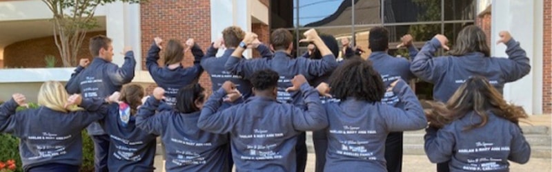 group of students from mock trial with team jackets facing back signaling to their jackets