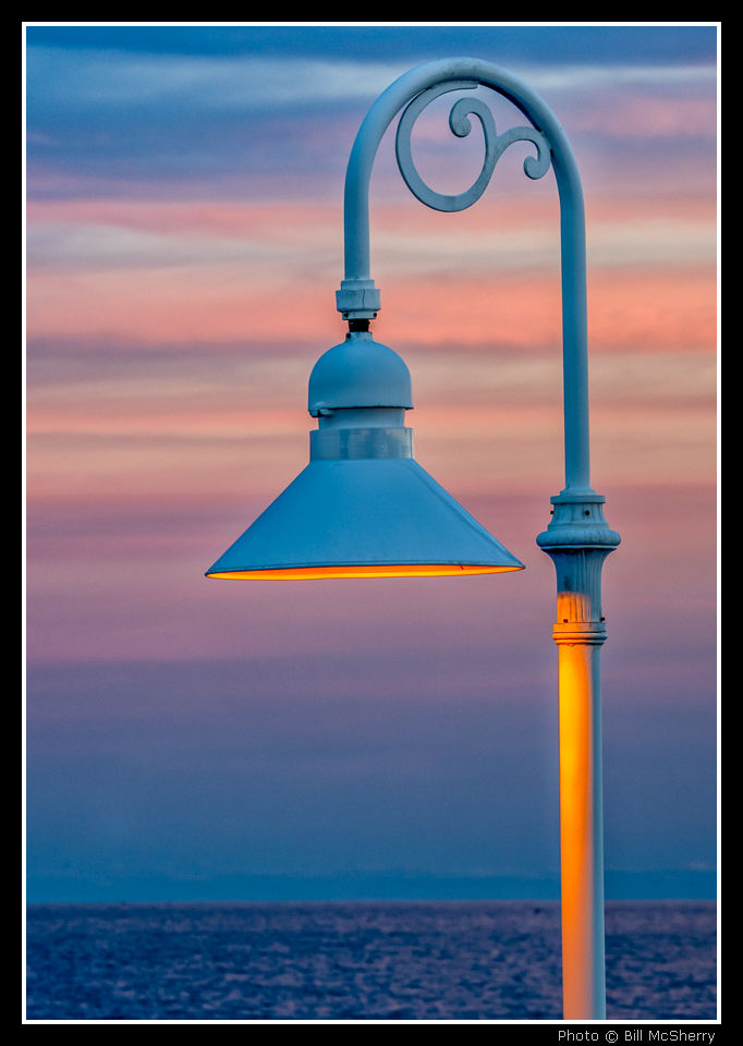 Artwork Product sample, a colored street lamp against a dusk sky with orange hues over the sea