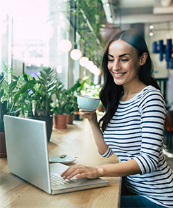 A student working on her laptop from a cafe while drinking coffee