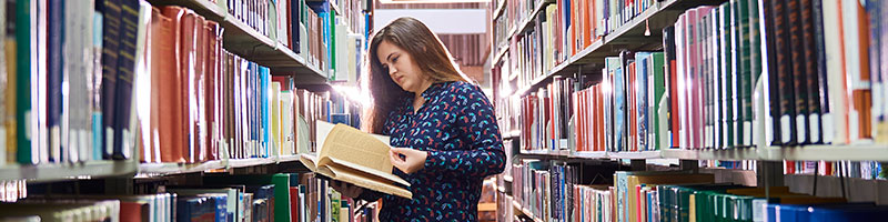 A student reading an open book in her hands at the library.