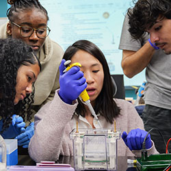 students in a lab gathered around professor doing experiment