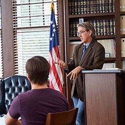 professor leaning on a lectern teaching class