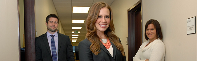 Student participant in clinic program stands next to two mentors in office hallway