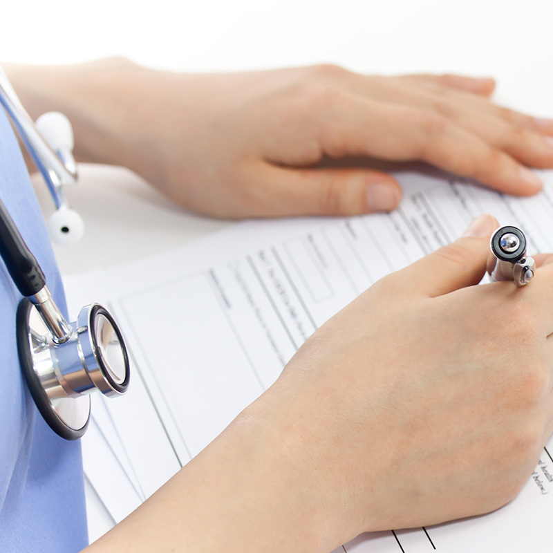 Person in scrubs wearing stethoscope writes on a paper