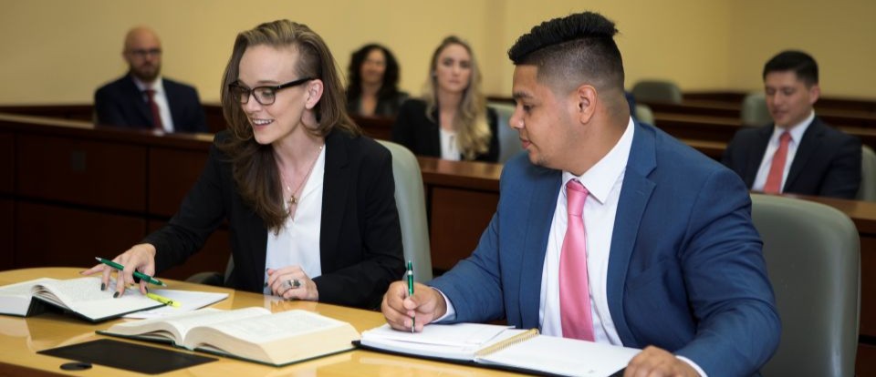 two students at a desk in a courtroom reviewing book materials