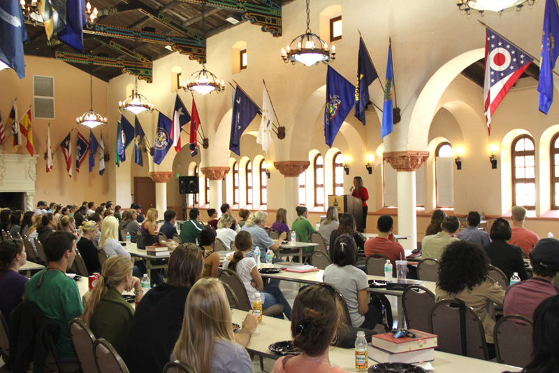 Students sitting in rows of tables in front of speaker