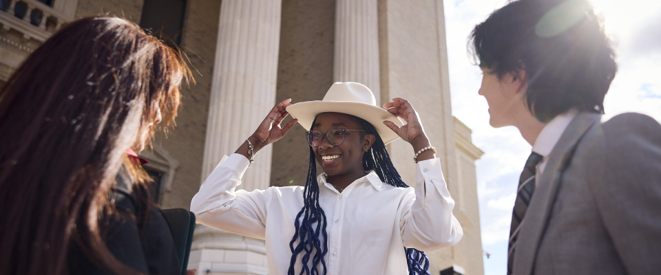 student  holding stetson hat in front of two students