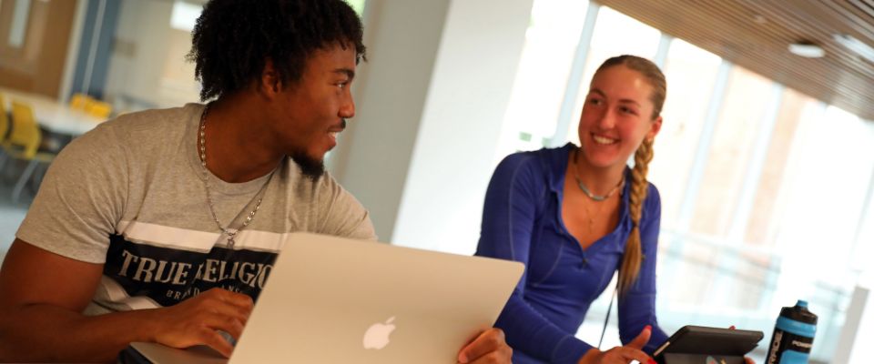 two students talking while using their laptops