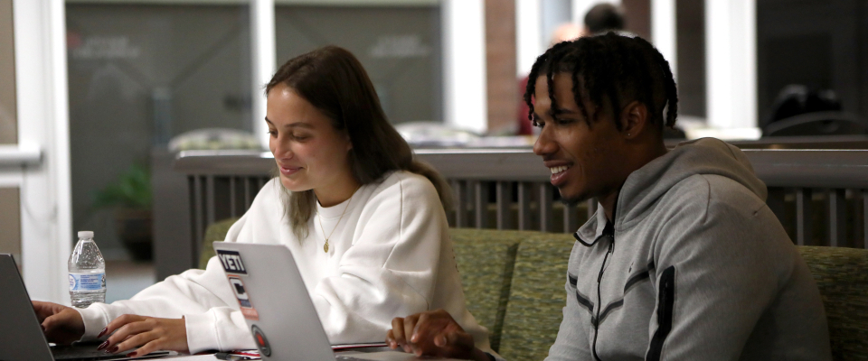 two students sitting next to each other using their laptops