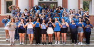 Bonner Scholars together wearing blue and making the 'Bonner love' signal with their hands in front of Sampson Hall