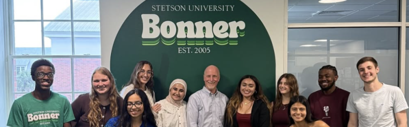 Students setting up for a photo in front of the Stetson University Bonner Program logo. 