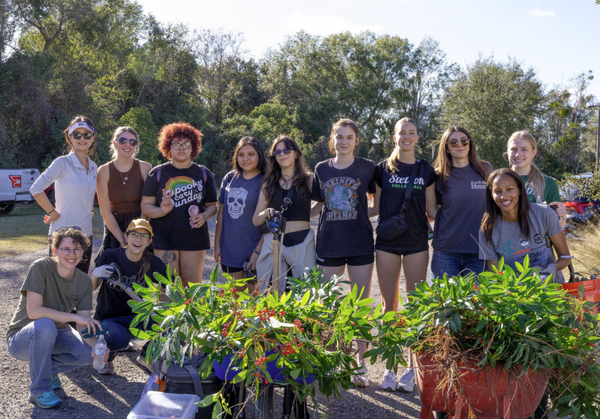 Students posing for photo behind a wheelbarrow of removed plants.