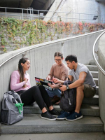 Three young adults sitting at the foot of stairs looking at a laptop