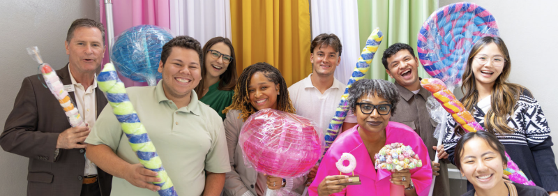A diverse group smiles while holding oversized colorful candy treats.