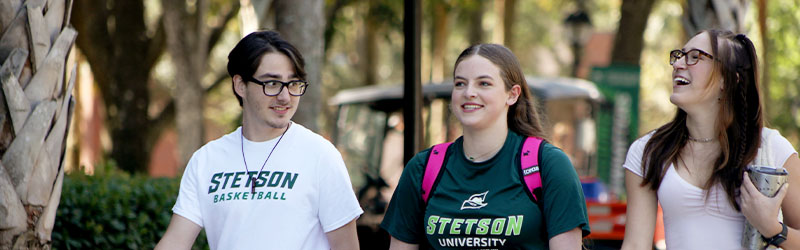 three smiling students walking and talking outside 