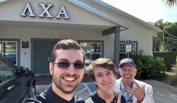 picture of three men in fornt of fraternity house