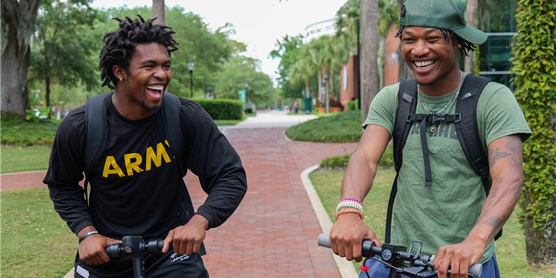 two students driving their scooters on campu