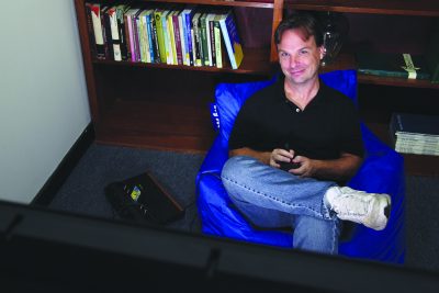 Chris Ferguson sits in a bean bag chair with a video game remote in front of a TV