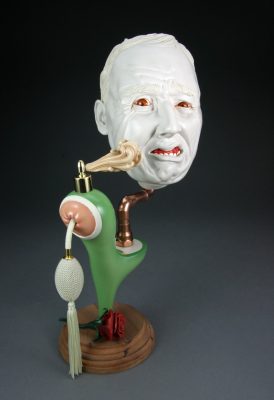 A ceramic face grimaces and sits atop a collection of objects, including a faucet on a pedestral.